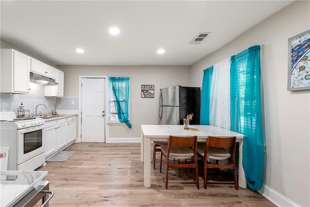 kitchen with white cabinets, white gas stove, stainless steel refrigerator, and light hardwood / wood-style floors