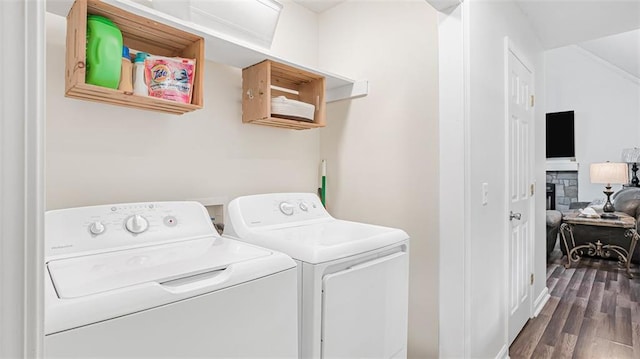 clothes washing area featuring hardwood / wood-style flooring, a stone fireplace, and washer and clothes dryer