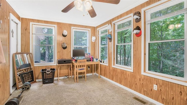 carpeted office space with ceiling fan, wooden walls, and crown molding