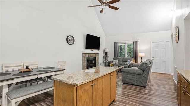 kitchen with a center island, high vaulted ceiling, ceiling fan, a fireplace, and light stone counters