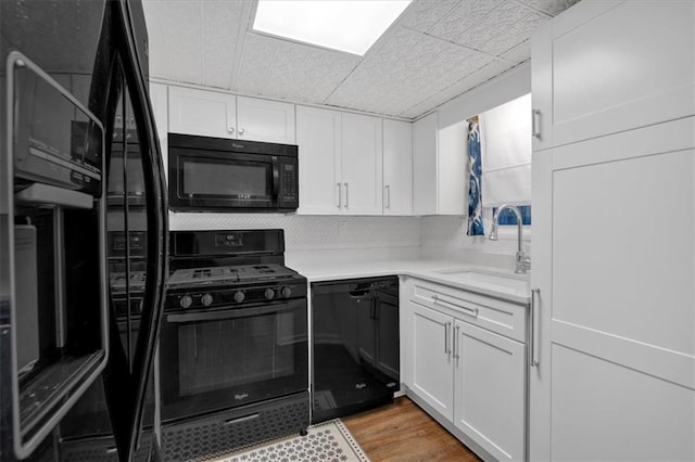 kitchen with light countertops, white cabinets, a sink, and black appliances