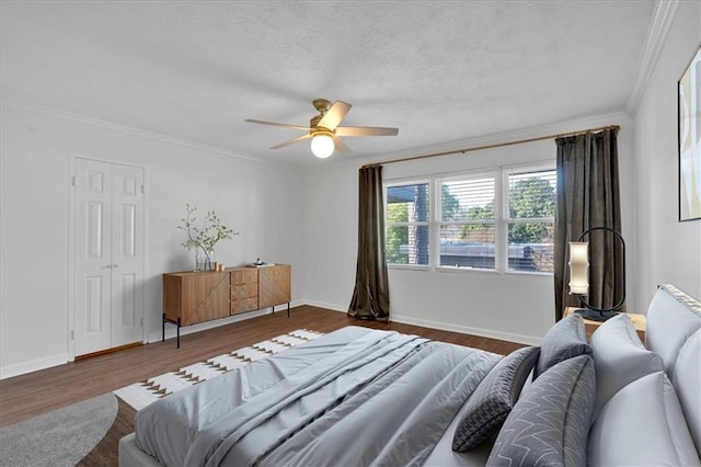 bedroom featuring crown molding, ceiling fan, a textured ceiling, wood finished floors, and baseboards