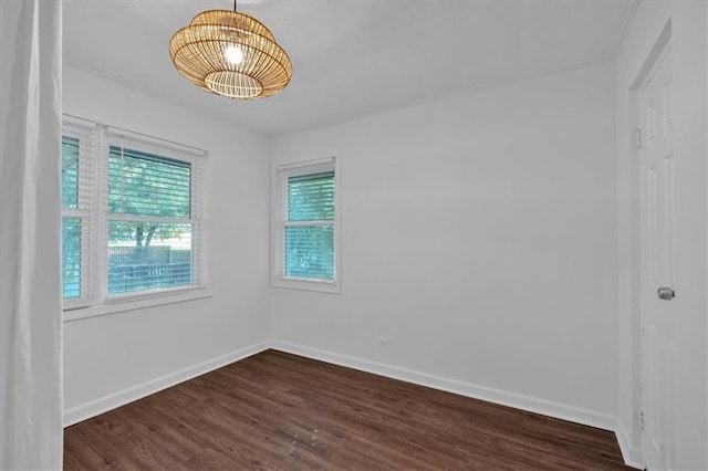 unfurnished room featuring baseboards, dark wood finished floors, and a notable chandelier