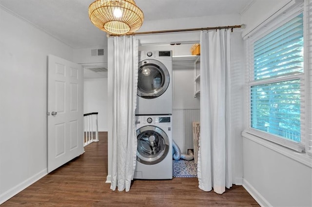 clothes washing area featuring stacked washer / drying machine, visible vents, wood finished floors, laundry area, and baseboards