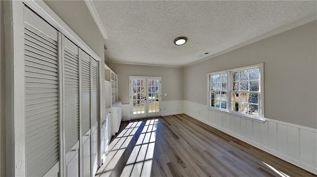 unfurnished bedroom featuring a closet, french doors, crown molding, and light wood-type flooring