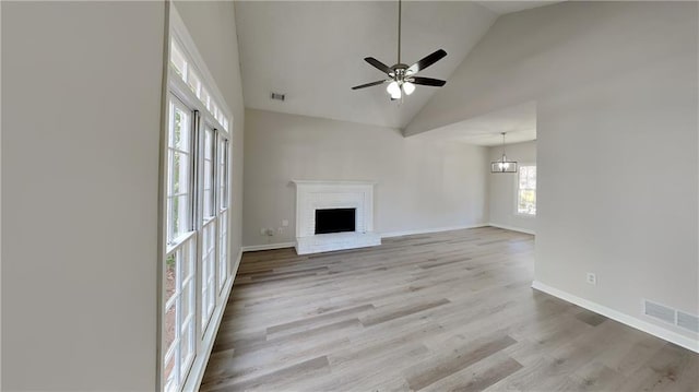 unfurnished living room featuring a fireplace, ceiling fan with notable chandelier, high vaulted ceiling, and light hardwood / wood-style flooring