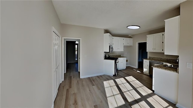 kitchen with white cabinets, range with electric stovetop, light hardwood / wood-style floors, and dark stone counters