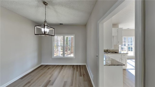 unfurnished dining area with a chandelier, sink, a textured ceiling, and light hardwood / wood-style flooring