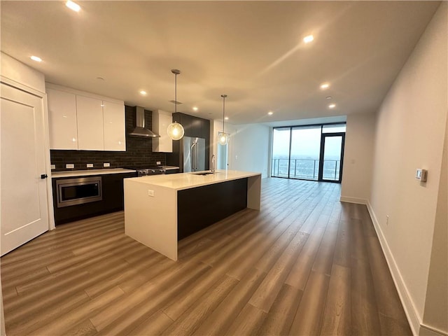 kitchen with light countertops, wall chimney exhaust hood, a sink, appliances with stainless steel finishes, and backsplash