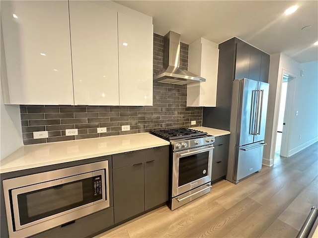 kitchen featuring wall chimney range hood, high quality appliances, light wood finished floors, gray cabinetry, and modern cabinets