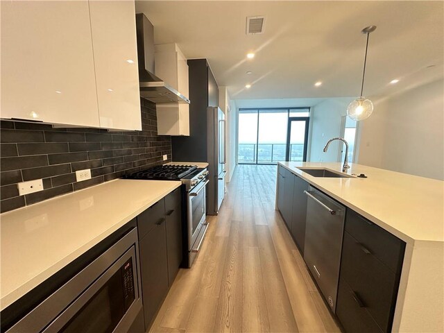 kitchen with wall chimney exhaust hood, stainless steel appliances, light wood-type flooring, visible vents, and modern cabinets