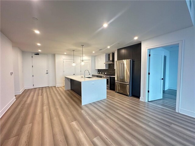 kitchen with wall chimney range hood, light countertops, tasteful backsplash, a sink, and appliances with stainless steel finishes