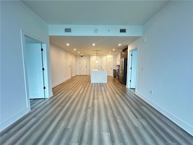 unfurnished living room with a sink, recessed lighting, baseboards, wood finished floors, and visible vents
