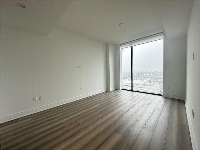 empty room featuring baseboards, a wall of windows, and dark wood finished floors