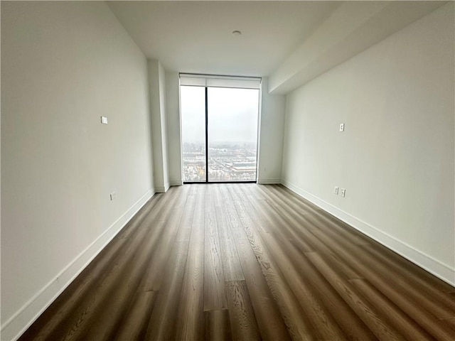 unfurnished room featuring dark wood-type flooring, baseboards, and a wall of windows