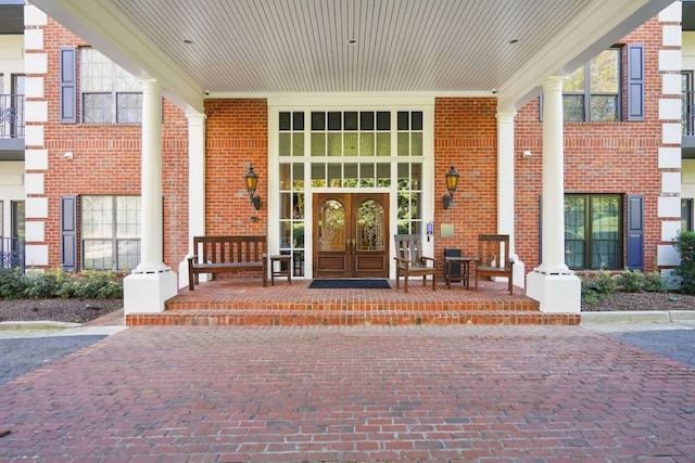 property entrance featuring brick siding, a porch, and french doors