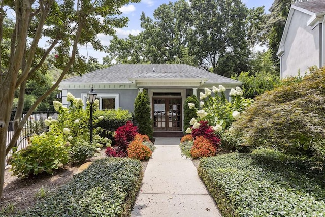 view of front of home with french doors, roof with shingles, fence, and stucco siding