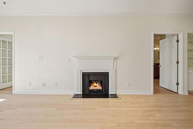 unfurnished living room with ornamental molding, a lit fireplace, baseboards, and wood finished floors