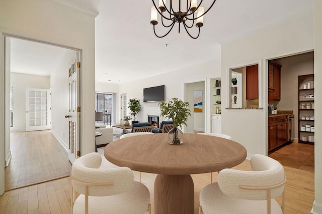 dining room featuring light wood-style floors, a lit fireplace, baseboards, and an inviting chandelier