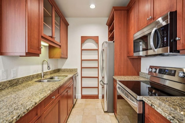 kitchen with light tile patterned flooring, a sink, appliances with stainless steel finishes, light stone countertops, and glass insert cabinets