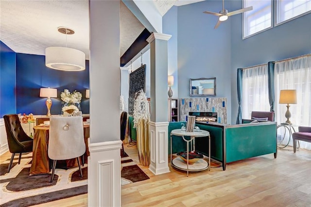 dining room featuring a glass covered fireplace, wood finished floors, a towering ceiling, and ceiling fan