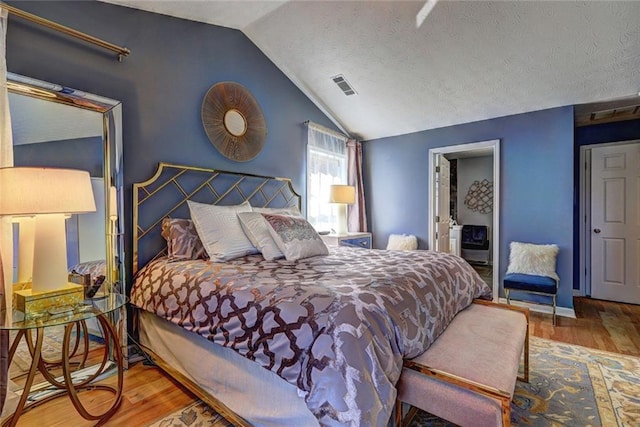 bedroom featuring visible vents, a textured ceiling, lofted ceiling, and wood finished floors