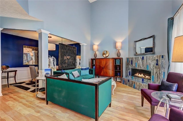 living area featuring ornate columns, a high ceiling, wood finished floors, and a warm lit fireplace