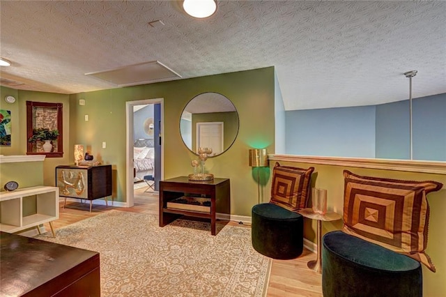 living area featuring a textured ceiling, attic access, baseboards, and wood finished floors