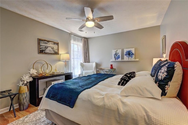 bedroom featuring a ceiling fan, baseboards, wood finished floors, visible vents, and a textured ceiling