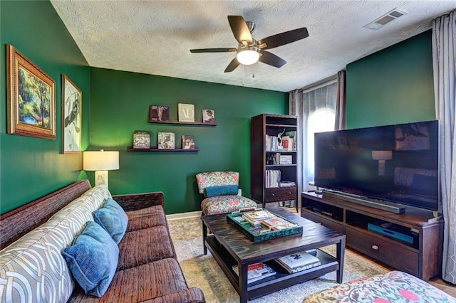 living area featuring visible vents, baseboards, a textured ceiling, and ceiling fan