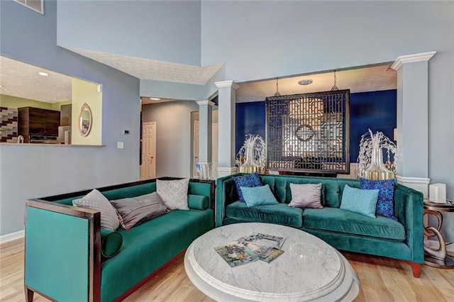 living area featuring baseboards, a high ceiling, ornate columns, and wood finished floors