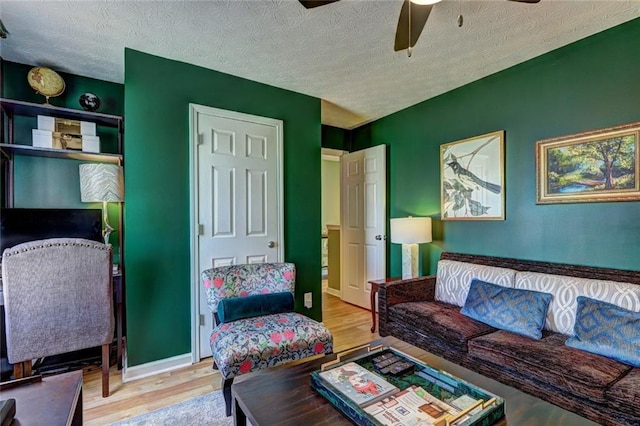 living area with ceiling fan, baseboards, a textured ceiling, and wood finished floors