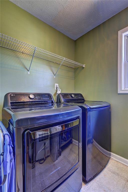 laundry area featuring laundry area, washing machine and dryer, a textured ceiling, and baseboards