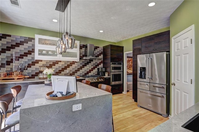 kitchen featuring visible vents, light wood-style flooring, dark brown cabinets, appliances with stainless steel finishes, and wall chimney exhaust hood