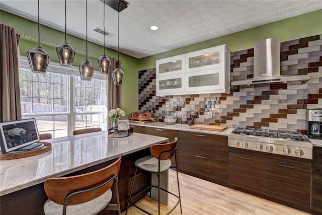 kitchen with visible vents, wall chimney range hood, light wood-type flooring, decorative backsplash, and stainless steel gas stovetop