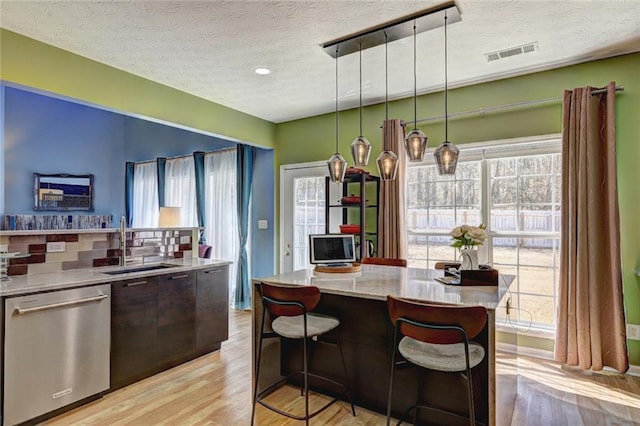 kitchen with a healthy amount of sunlight, visible vents, a sink, light wood-style floors, and stainless steel dishwasher