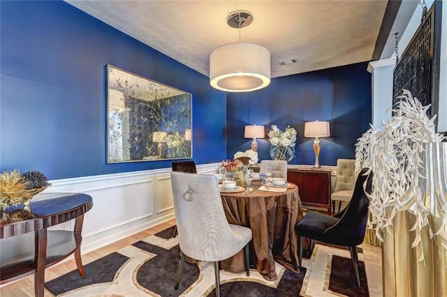 dining area with visible vents, wood finished floors, a wainscoted wall, and a textured ceiling