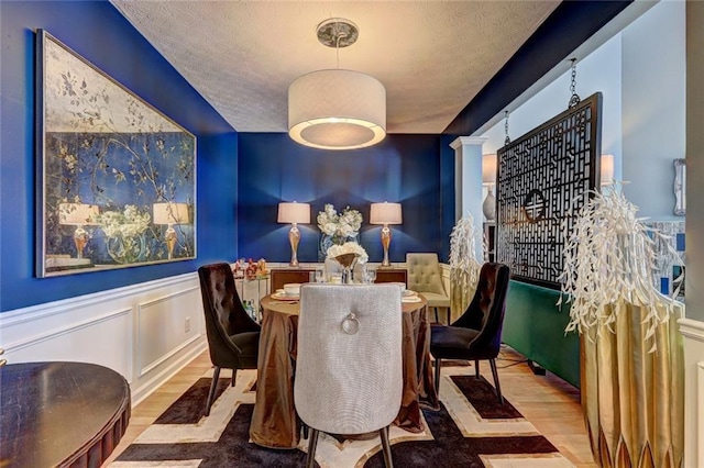 dining area featuring a textured ceiling, wood finished floors, wainscoting, and a decorative wall