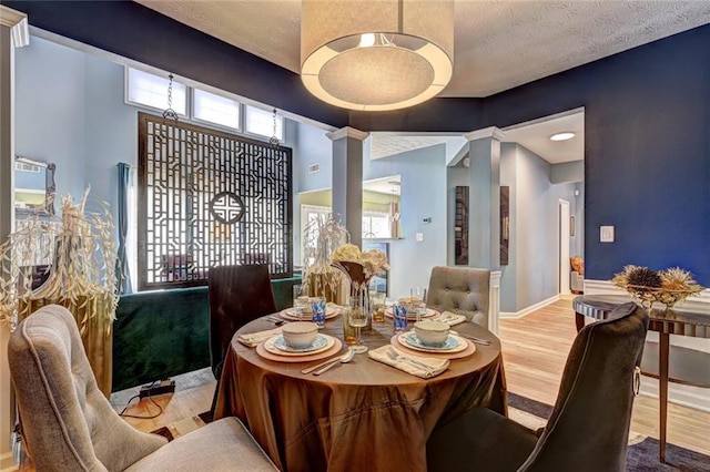 dining space with a textured ceiling, wood finished floors, baseboards, and decorative columns