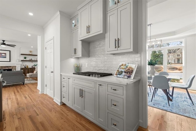 kitchen featuring a fireplace, tasteful backsplash, stainless steel gas stovetop, ceiling fan, and light wood-type flooring