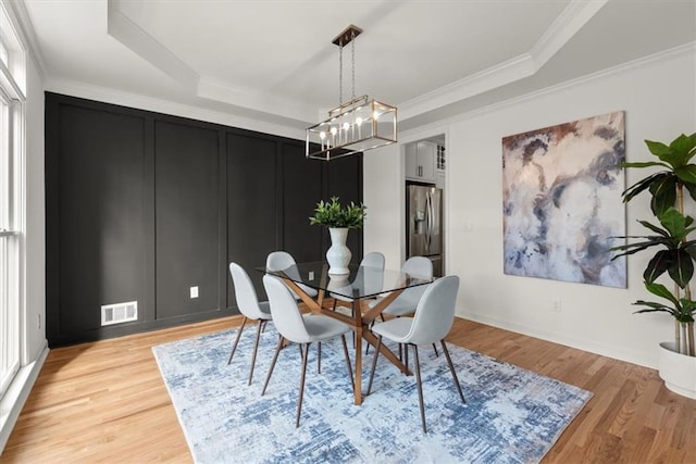 dining space with crown molding, a raised ceiling, and light hardwood / wood-style flooring