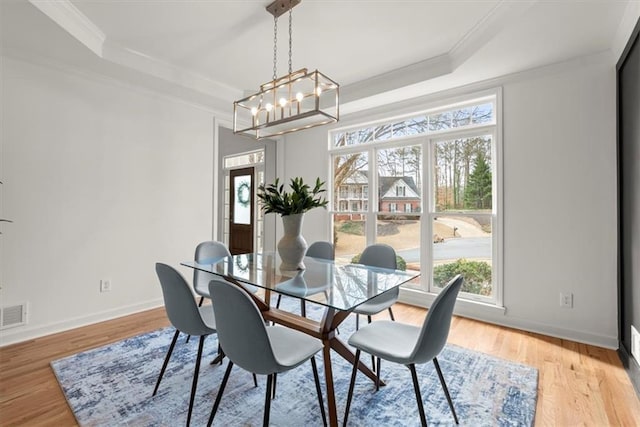 dining space featuring a notable chandelier, a tray ceiling, ornamental molding, and light hardwood / wood-style floors