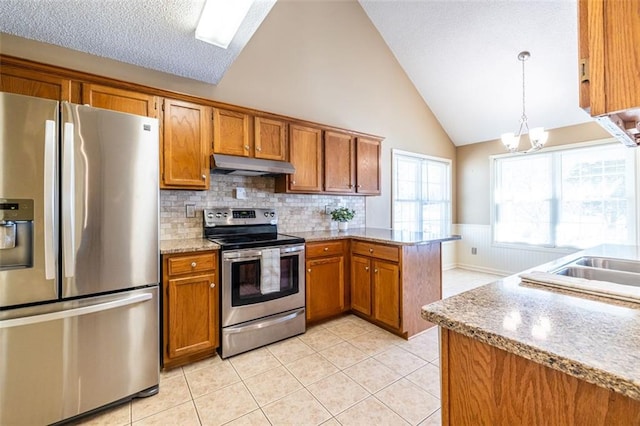 kitchen featuring a wainscoted wall, brown cabinets, stainless steel appliances, under cabinet range hood, and pendant lighting