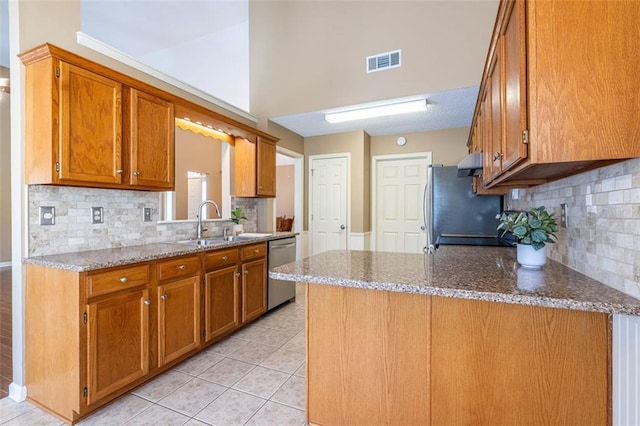 kitchen with visible vents, brown cabinetry, stainless steel appliances, stone counters, and a sink