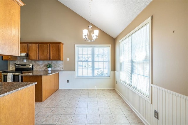 kitchen with wainscoting, dark countertops, hanging light fixtures, stainless steel range with electric stovetop, and light tile patterned flooring