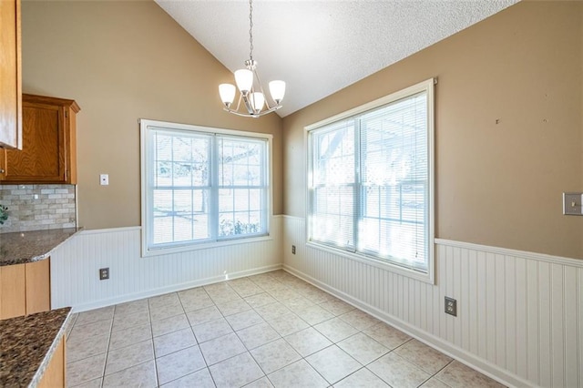 unfurnished dining area featuring lofted ceiling, a wainscoted wall, a textured ceiling, a chandelier, and light tile patterned flooring