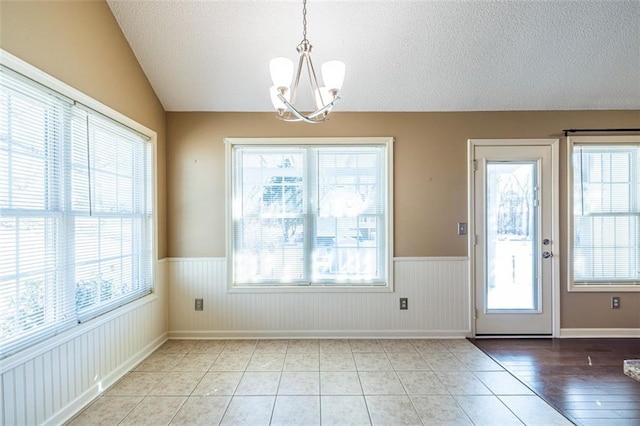 interior space featuring a wainscoted wall, vaulted ceiling, a textured ceiling, and an inviting chandelier