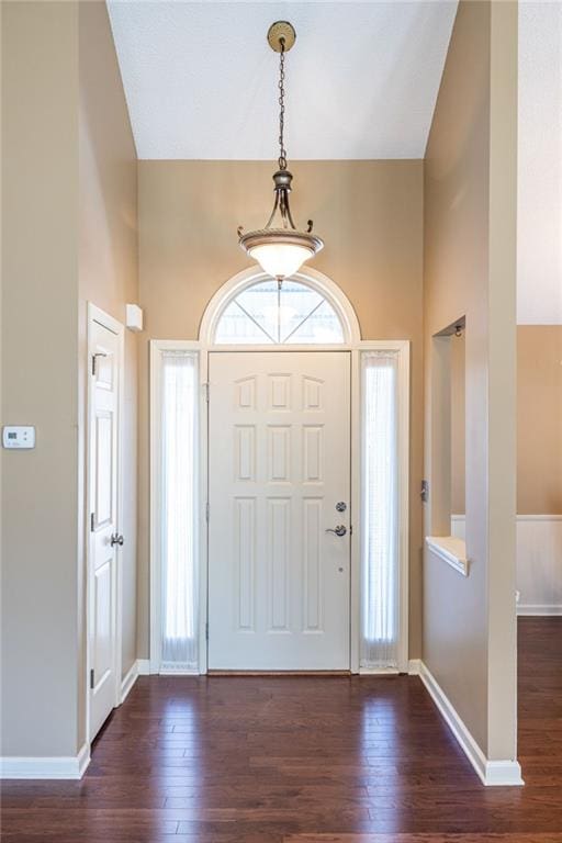 entrance foyer with dark wood finished floors, a towering ceiling, and baseboards