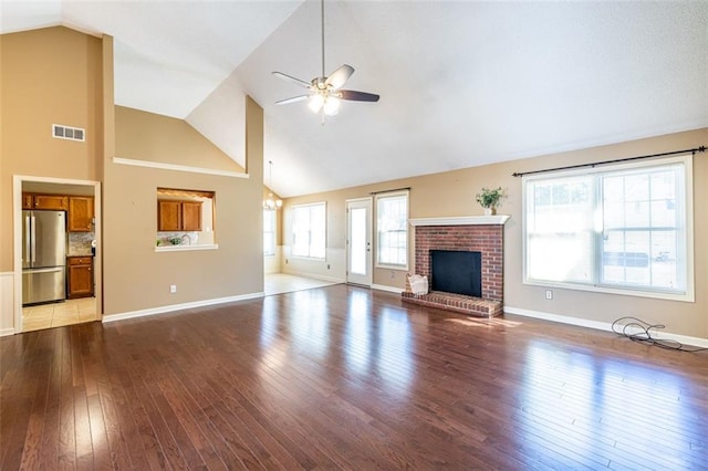 unfurnished living room featuring ceiling fan with notable chandelier, a fireplace, visible vents, baseboards, and light wood finished floors