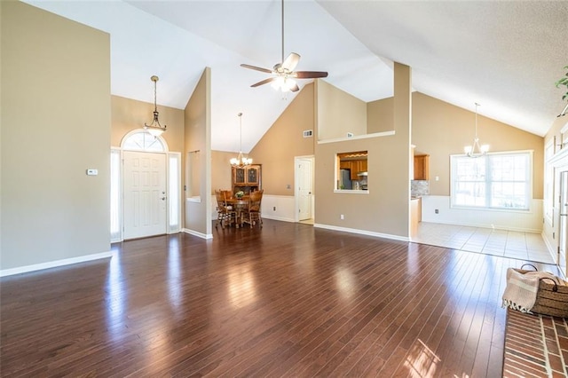 unfurnished living room featuring ceiling fan with notable chandelier, high vaulted ceiling, wood finished floors, and baseboards